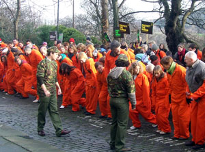 Demonstrators in orange boiler suits are commanded to get down in front of the US Consulate in Regent Terrace, Edinburgh
