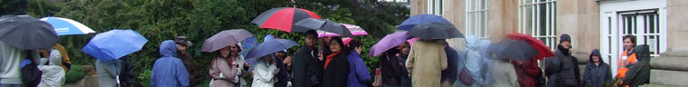 Line of people with blue, red, black and purple umbrellas waiting outside the Glass House