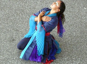 A dancer in blues and purples kneels grieving the trickster figure