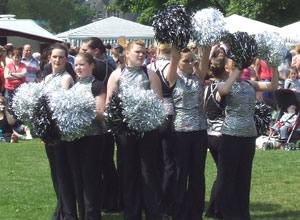 Young women in black slacks and silver tops shake silver and black pom poms