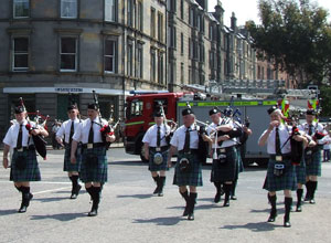 Pipers marching in formation with a passing fire engine in the background