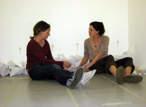 Two women sit working together with Scotmid bags full of figures behing them