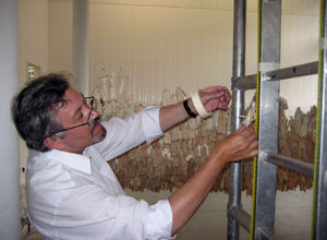 Man measure a figure against a yellow tape running down the scaffolding