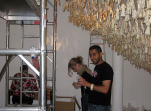 Two people standing beneath dangling figures as they bubble wrap two more figures