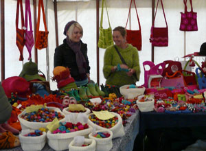 Two smiling women behind a stall of small felt items coloured yellow, pink, red, orange, turquoise, and lime green