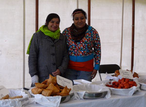 Two women smiling behind a table filled with samoas and pakoras