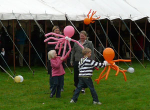 Two children playing with pink and orange octopus balloons, as their Mums watch on