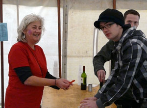 Smiling Tannis in a red t-shirt, handing over a ticket at the wine stall