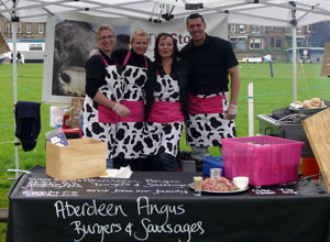 Three smiling women and a man in black and white hoof print aprons with shocking pink sashes