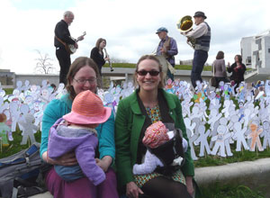 Two women with babies sittting amongst the paper figures with a four  piece band playing in the background