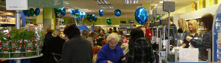 An elderly woman in a blue coat leavign the checkout