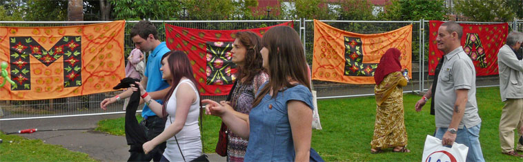 Visitors pass four red and orange tapestries, spelling out the letter M, E, L and A