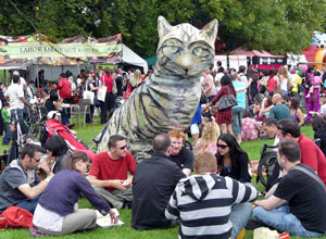 Group of people seated on the grass round a six foot high sculpture of a tabby cat