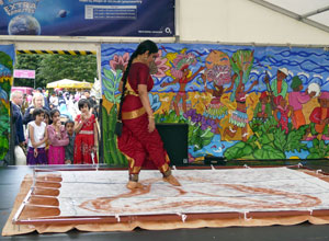 Ananda in red with gold trim painting a white canvas with her feet as she dances