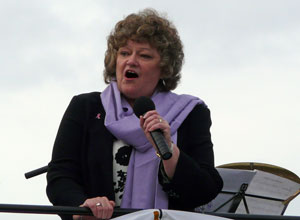 Cathy Peattie with a lilac scarf singing from the open top bus