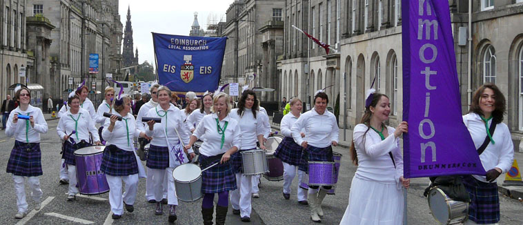 Commotion marching with drums  down  Waterloo Place wearing white with purple tartan kilts