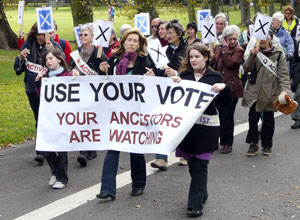 Two girls and a woman carrying a banner "Use your Vote: Your ancestors are watching"