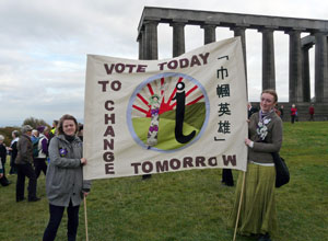 Two women hold the Vote Today to Change Tomorrow banner with the columns of the Folly in the background