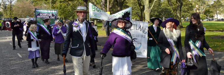 Marchers in Edwardian dress with lilac and green ribbons entering Middle Meadow Walk