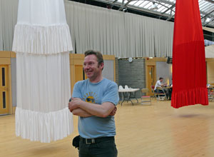 Man in blue tee shirt with arms folded between the foot of a 50' white ball dress and the foot of a 50' red ball dress