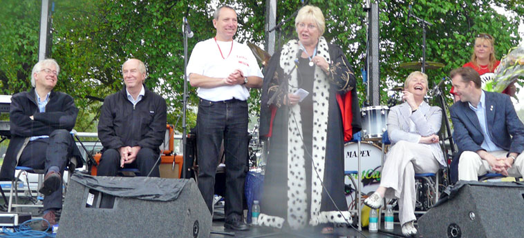 Margo Macdonald in black robes with mock ermine trim, speaking from the stage
