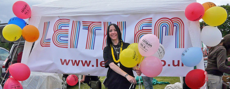 Pam McNamee of Leith FM in front of a Leith FM banner with balloons