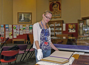 Woman wearing white gloves looking at  a  book larger than A4 size