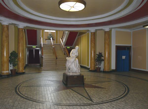 A tiled floor with a six pointed star, that has a  marble statue in the centre leading under a round ceiling to a staircase