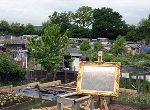 Gold framed picture on easel with allotments and trees behind it