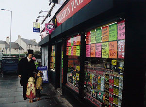 Cardboard cut out of Rev Guthrie with small children outside store with cans of alcohol stacked in the window