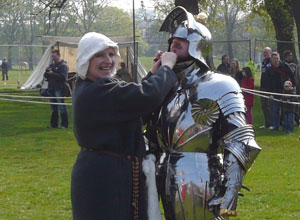 A woman ties on the helmet of a fully armoured Rennaissance Era knight