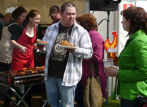 Woman in a red apron serving sausages and a man with paper plates of sausage and vegetables