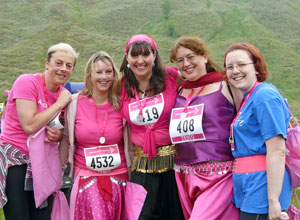 Five smiling women in shocking pink, purple and blue with Salisbury crags behind