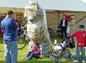 Girl sits between the paws of a giant papier mache tabby cat commissioned for the Edinburgh MELA