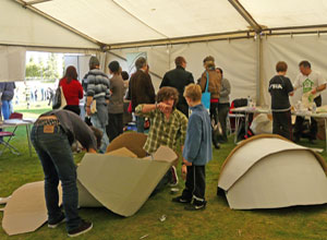 Two young men constructing a giant cardboard ball, as a boy stands watching