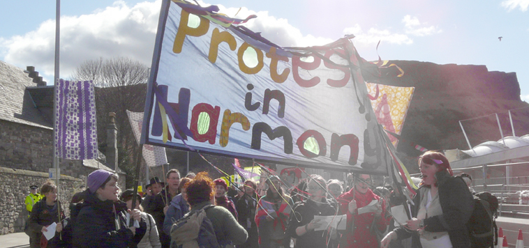 Protest in Harmony with their banner set against the backdrop of Salisbury  Crags