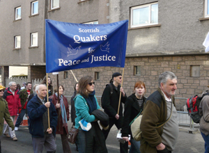 Quakers marching under the blue banner with white text: "Scottish Quakers for Peace and Justice