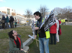 Woman sitting with a  book on the  grass terraces talking to a  man with placards