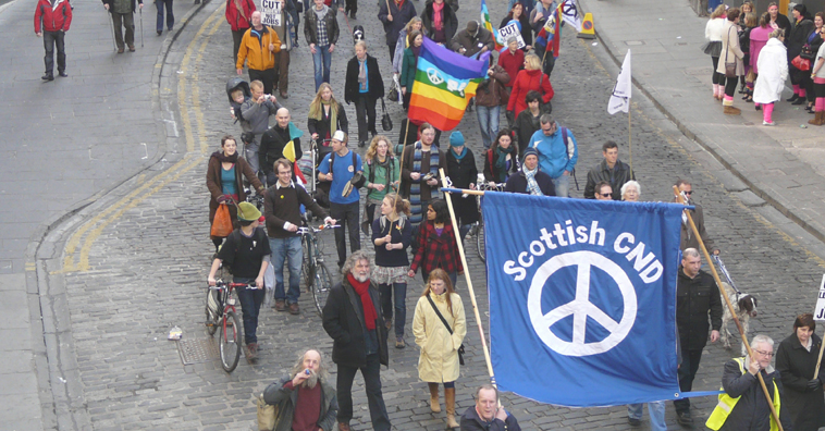 View of march from above, as it walks down Victoria St, a blue Scottish CND banner in the foreground