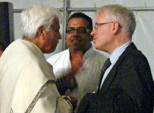 Two men in white speaking to man in black suit