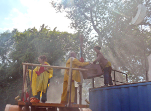 Man in fisherman's clothes hands suitcase up from his boat to woman on blue transport container, while his companion tends to their fish