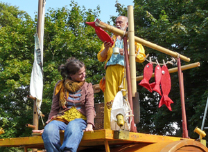 Woman sitting on the edge of a yellow boat as a man in yellow waterproofs hangs red fish on a line on the end of his boat