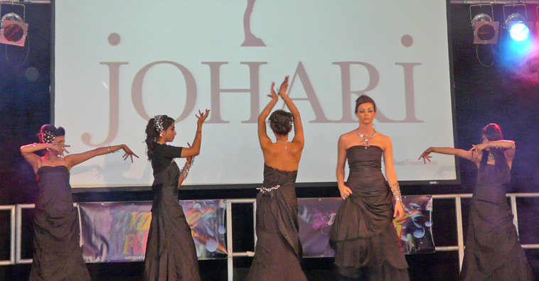 Five women in black strapless evening dresses holding their arms up to show off jewellery