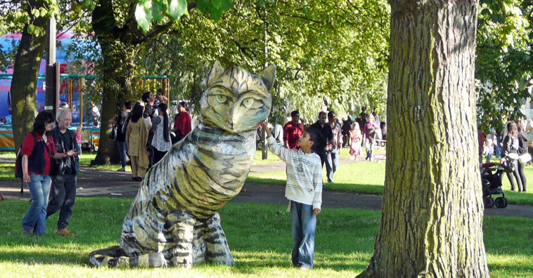 A boy strokes the giant papier mache tabby cat under the trees od Leith Links as  visitors pass by
