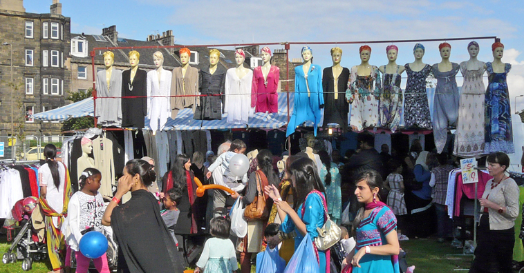 People walking past a stall with 15 women tailors dummies suspended above it