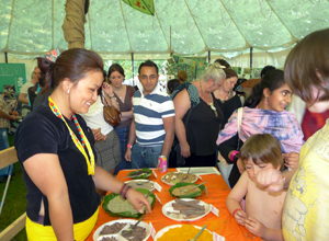 Smiling woman in black and yellow showing children plates of spices