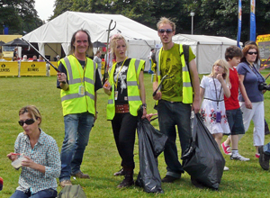 Two men and a woman in yellow jackets holding up their litter pickes