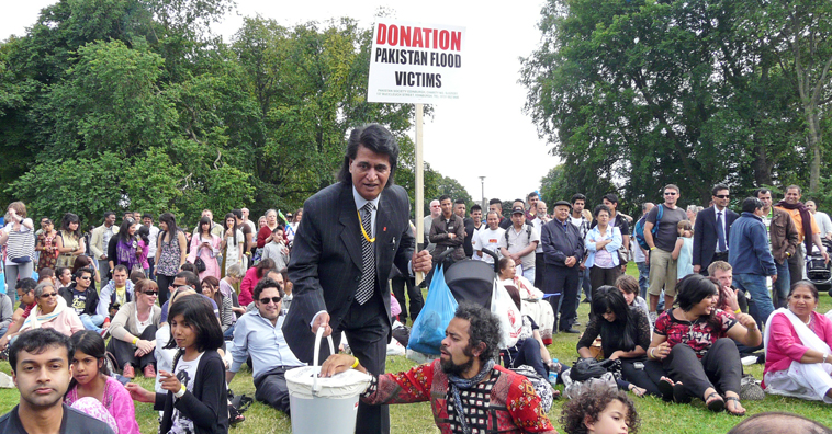 Seated man puts money in bucket collecting donations for Pakistan  flood victims being collected by charcoal suited Shami Khan