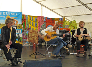 Three men seated, Ilhan Barutcu, playing a woodwind instrument the others playing guitars