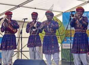 Four men playing brass instruments wearing turbans, purple embroiderd coats and white breeches